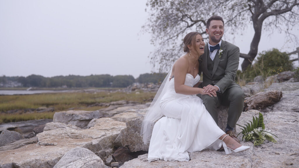 humblebee wedding videography wentworth by the sea, couple sits beside harbor embracing and laughing