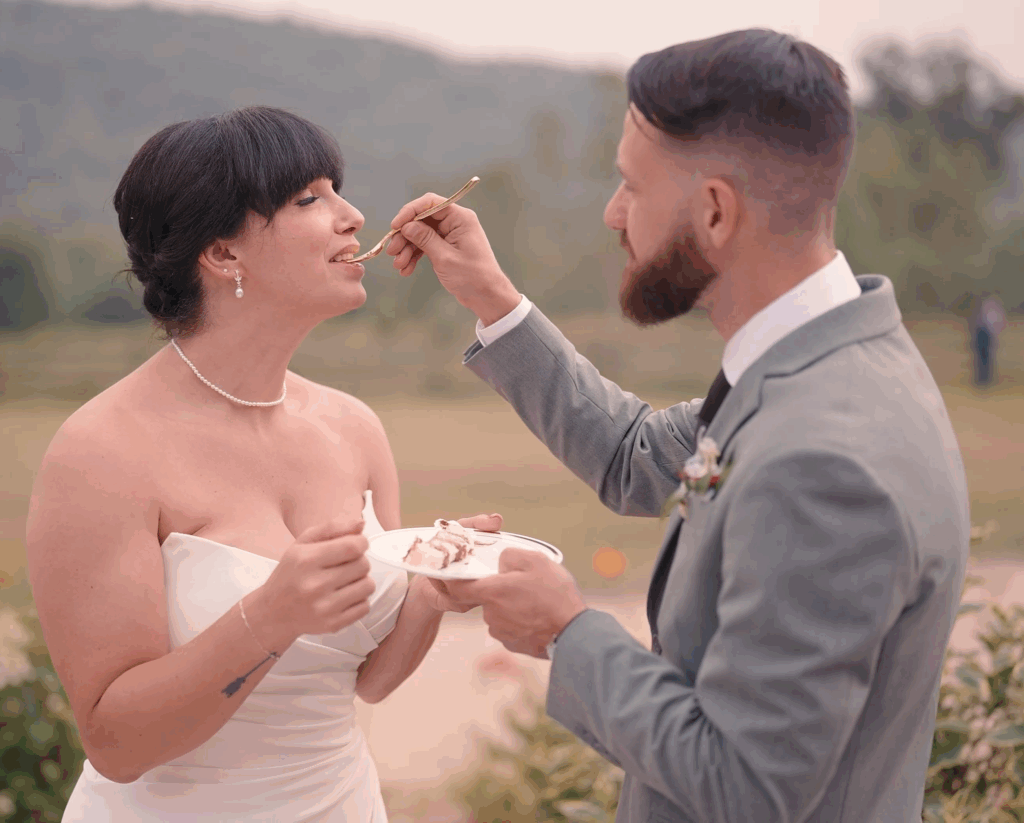 Humblebee Wedding Videography Cold Spring Farm, groom feeds bride cake with farmland behind them