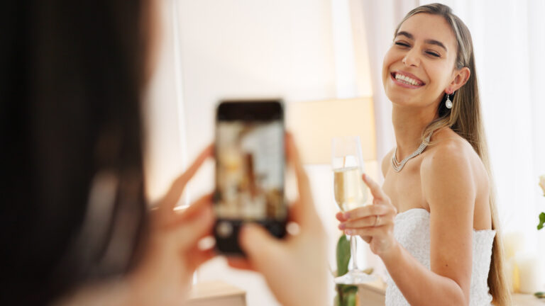 Humblebee Wedding Films Boston wedding content creator, Smartphone photography of bride with champagne glass for wedding celebration to post on social media app. Smile portrait photos or picture taken of woman on digital cellphone and celebrate with wine.