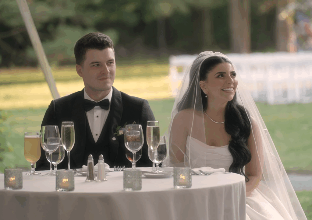 Humblebee Wedding Films Boston wedding content creator, newly weds sit at newly wed table and smile at photographer