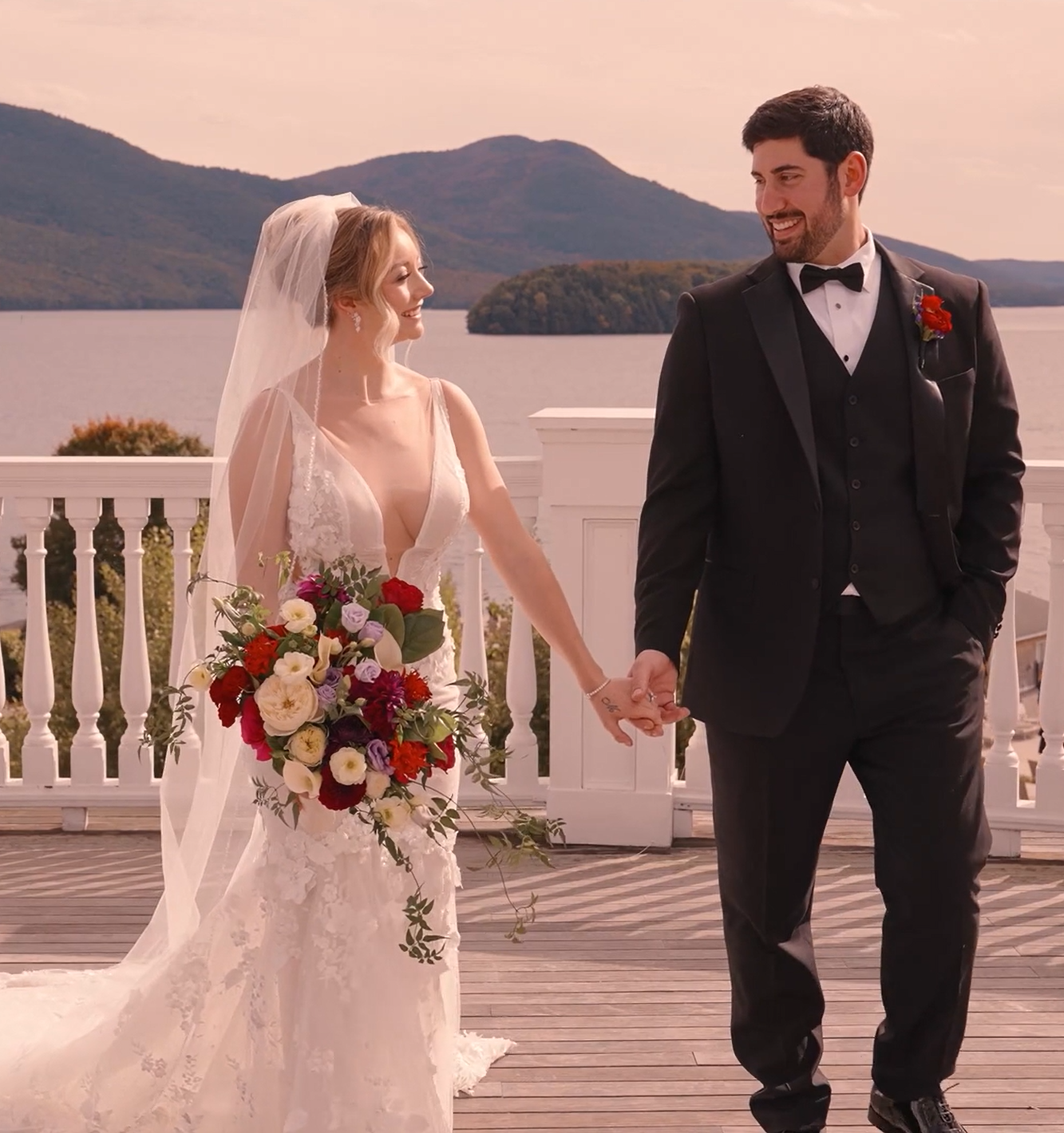 Humblebee Wedding Films Wedding Videography Videos, bride and groom look at each other and walk towards camera hand in hand, lake in background