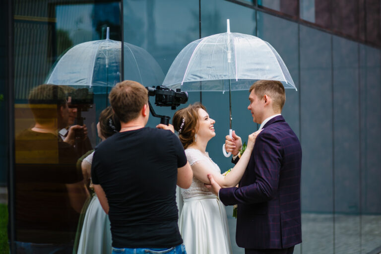 Humblebee Wedding Films Large Wedding Videography Studio, Professional wedding videographer shoots a movie with the newlyweds under an umbrella next to a glass wall