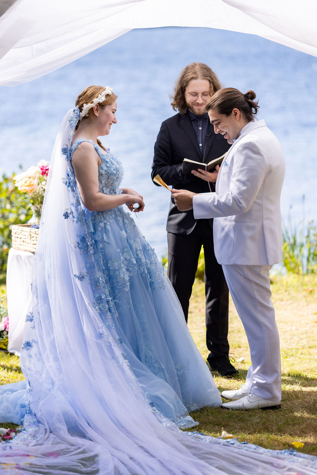 Humblebee Wedding Films Videographers for Weddings Near me, couple exchanges vows at a floral and tulle adorned altar with a body of water behind them
